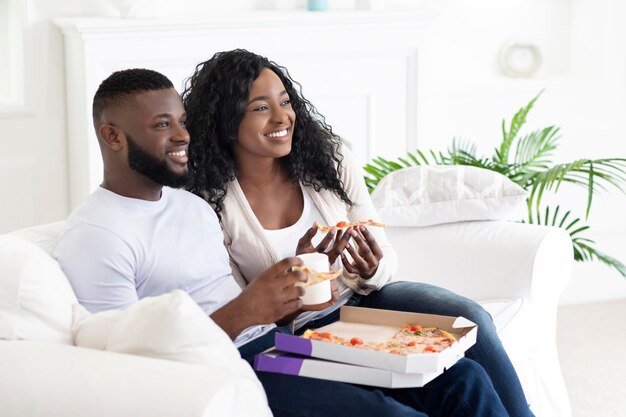 Dia de folga em casa. Casal de família negra comendo pizza e bebendo café, passando o fim de semana juntos.