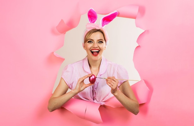 Dia de páscoa mulher feliz em orelhas de coelho espreitando através de papel sorrindo mulher coelho pintando ovo