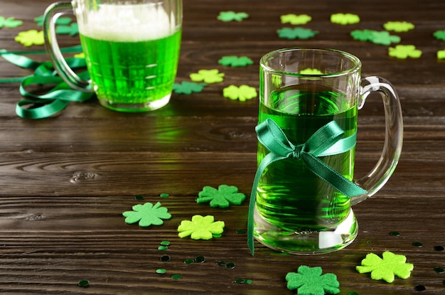 Dia de São Patrício conjunto com uma caneca de cerveja verde em uma mesa de madeira com trevos de feltro artesanais. Espaço para cópia