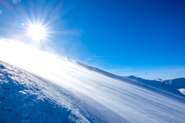 Dia de sol de inverno. pista de esqui vazia. um vento forte levanta uma grande quantidade de poeira de neve que brilha ao sol