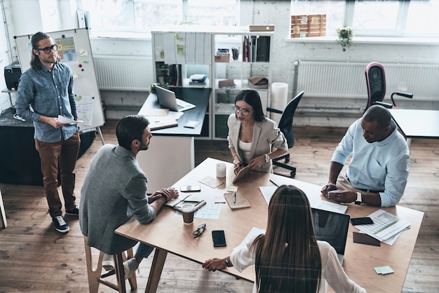 Dia de trabalho agitado. Vista superior de jovens empresários se comunicando enquanto trabalham juntos na sala da diretoria