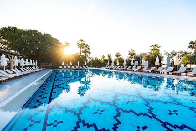 Dia de verão perfeito em um resort de luxo com espreguiçadeiras e guarda-sóis esperando por uma piscina cristalina cercada por uma vegetação luxuriante