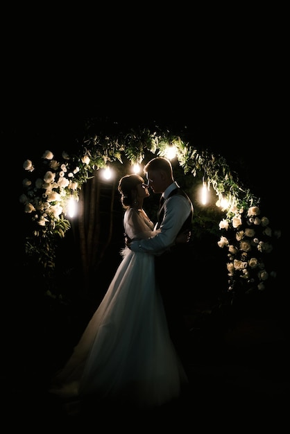 Dia do casamento dos votos noturnos dos noivos perto do arco com luzes no fundo dos fogos de artifício