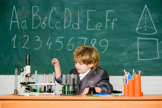 Dia do conhecimento Conhecimento básico educação primária Infância feliz Criança gosta de estudar Conceito de conhecimento Menino perto de microscópio e tubos de ensaio na sala de aula Criança estuda biologia química