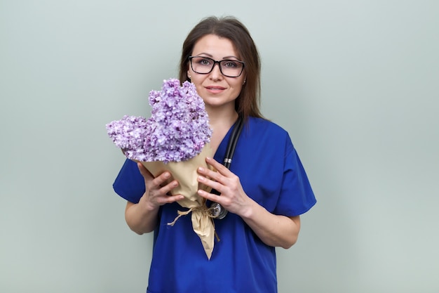 Dia do Médico, comemoração. Médica sorridente feliz com buquê de flores, posando de mulher olhando para a câmera, fundo verde claro