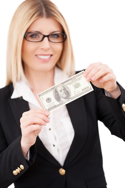 Dia do pagamento! Mulher de negócios confiante e madura estendendo as mãos com uma nota de cem dólares e sorrindo em pé isolado no branco