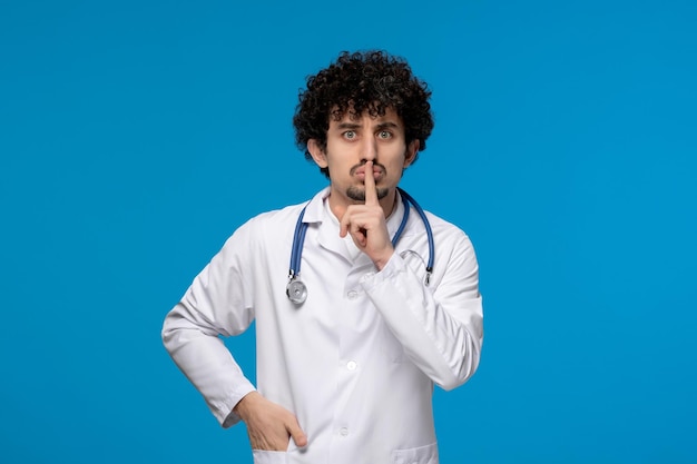 Dia dos médicos cara bonito e bonito em uniforme médico fazendo gesto de silêncio