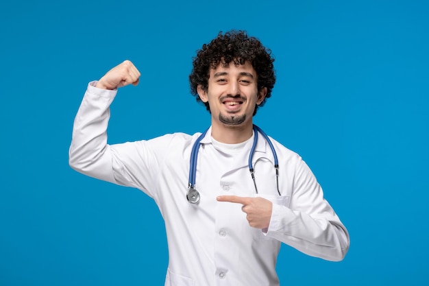 Dia dos médicos cara bonito e bonito em uniforme médico mostrando seu bíceps