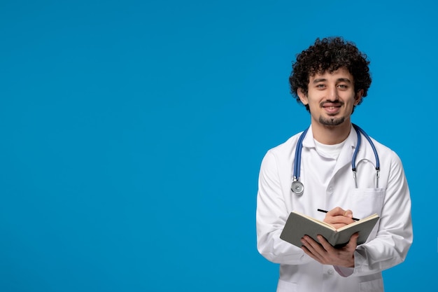 Foto dia dos médicos cara bonito e bonito em uniforme médico sorrindo e escrevendo uma nota