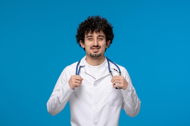 Dia dos médicos cara bonito e bonito em uniforme médico sorrindo e segurando um estetoscópio