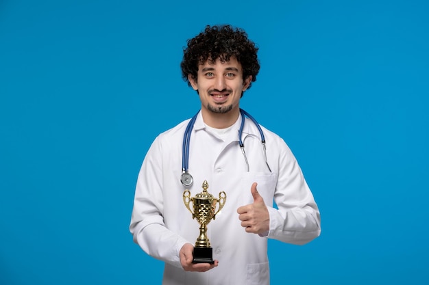 Dia dos médicos cara bonito e bonito em uniforme médico sorrindo e segurando um troféu