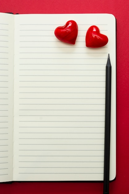 Dia dos namorados. Abra o caderno com corações vermelhos e um lápis, sobre fundo vermelho, copie o espaço para texto.