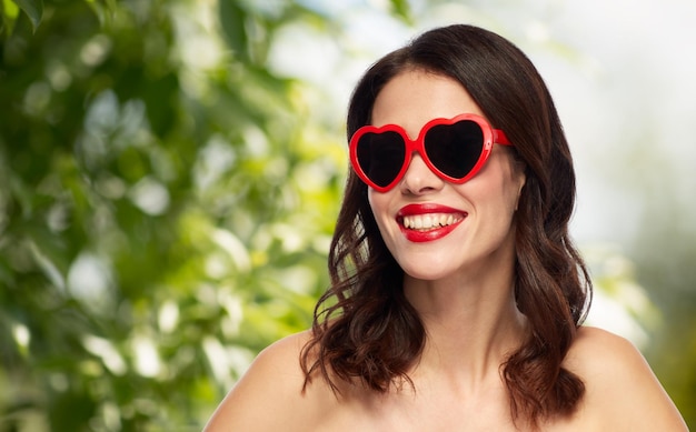 Foto dia dos namorados beleza e pessoas conceito feliz sorridente jovem mulher com batom vermelho e óculos de sol em forma de coração sobre fundo verde natural