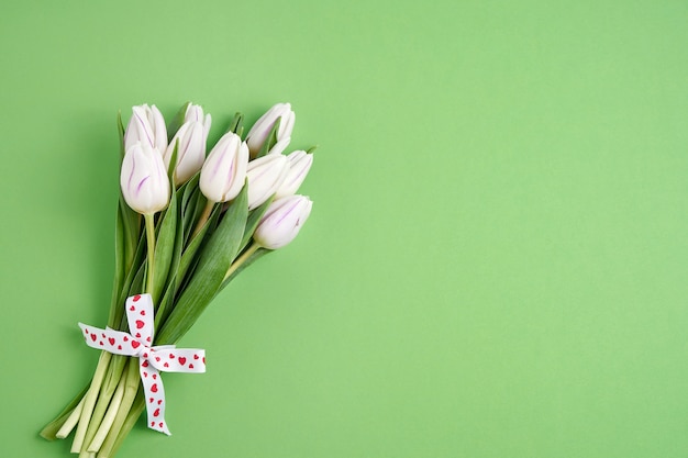 Dia dos namorados, conceito de aniversário. ramalhete branco das tulipas decorado com a fita dos corações no fundo verde. copie o espaço, vista superior