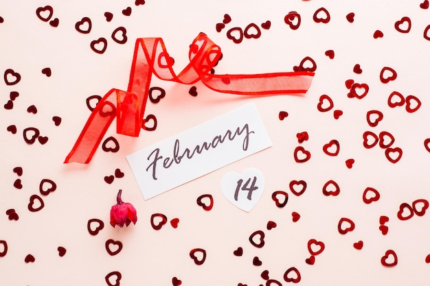 Dia dos namorados. Data de 14 de fevereiro, flor seca e fita vermelha em fundo rosa com corações espalhados
