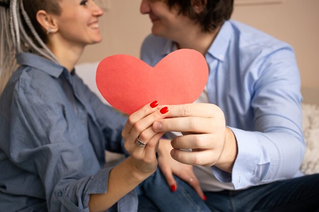 Dia dos namorados de coração vermelho. Lindo casal jovem no quarto sentado na cama e se abraçando.