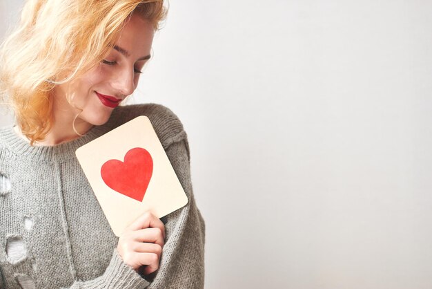 Dia dos Namorados. Jovem camisola segurando um cartão com um coração. Em um fundo cinza