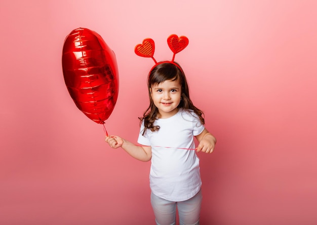 Dia dos namorados, menina segurando um grande balão em forma de coração em um fundo rosa.
