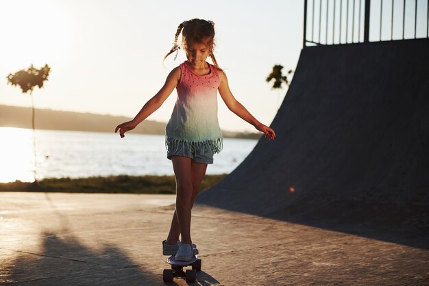 Dia ensolarado. Garoto se diverte com o skate na rampa. Menina alegre.