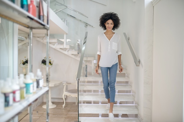 Día excelente. Niña sonriente en ropa casual bajando escaleras en el centro de belleza