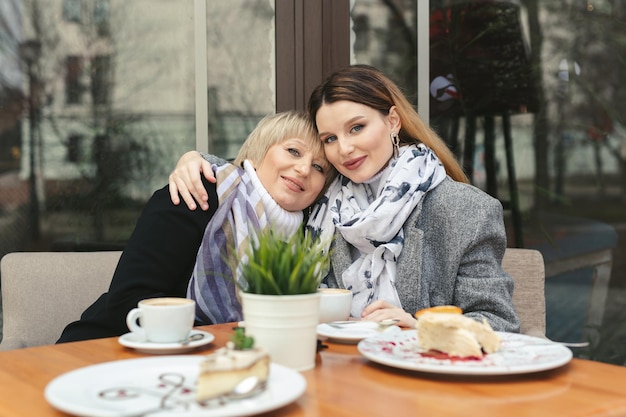 Foto dia familiar. una anciana y su hija adulta toman café en un café en la acera y se abrazan. retrato familiar.