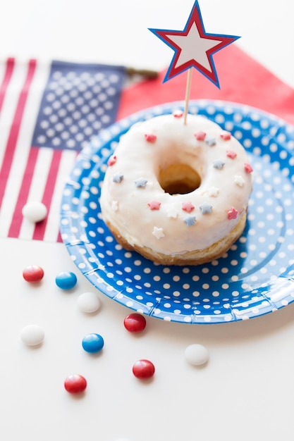 día de la independencia americana, celebración, patriotismo y concepto de vacaciones - cierre de donut dulce glaseado con bandera americana y decoración de estrellas en plato desechable en la fiesta del 4 de julio desde arriba