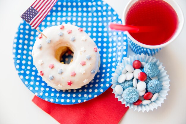 día de la independencia americana, celebración, patriotismo y concepto de vacaciones - cierre de donut dulce glaseado con jugo y dulces en vajilla desechable en la fiesta del 4 de julio desde arriba