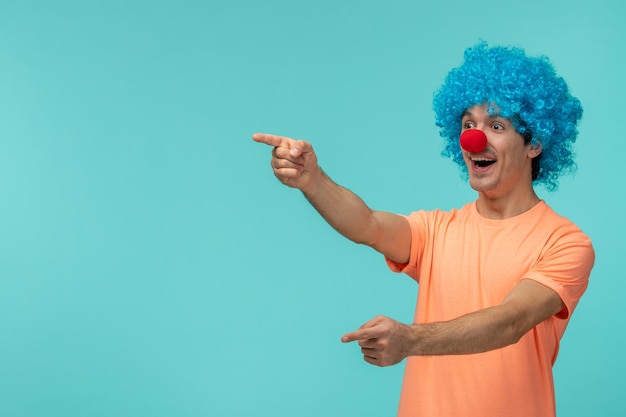 Día de los inocentes chico payaso bromeando riendo señalando con el dedo cabello azul emocionado gracioso broma nariz roja