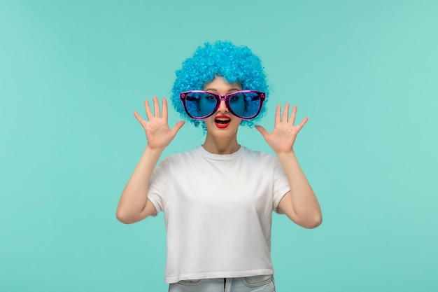 El día de los inocentes sorprendió a la chica del payaso con las palmas hacia arriba, grandes gafas de sol azules y rosas, disfraz divertido, cabello azul.