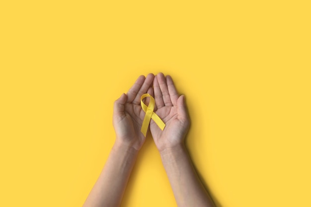 Foto día internacional del cáncer infantil manos del niño sosteniendo una cinta amarilla conciencia sobre el sarcoma