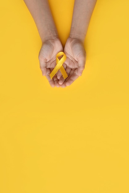 Foto día internacional del cáncer infantil manos del niño sosteniendo una cinta amarilla conciencia sobre el sarcoma