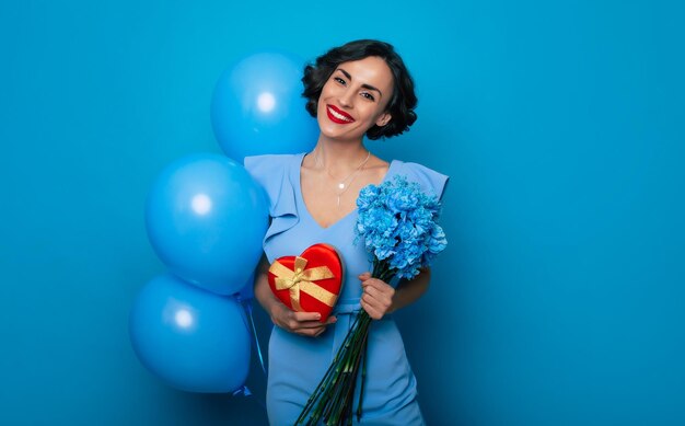 Dia Internacional da Mulher Dia das Mães Dia dos Namorados Linda mulher feliz em um vestido azul segura um monte de flores da primavera e balões que ela recebe em suas mãos de seu amado