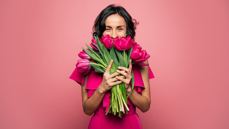 Foto dia internacional da mulher. uma mulher extremamente feliz em um vestido rosa brilhante está cheirando um ramo de flores da primavera, que está segurando nas mãos.