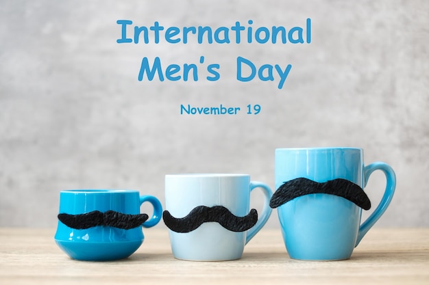 Día internacional del hombre con taza de café azul o taza de té y decoración de bigote negro en la mesa. Feliz día del padre y concepto de celebración