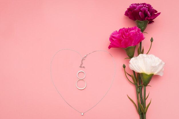 Día Internacional de la Mujer con flores y collar con forma de corazón sobre fondo rosa