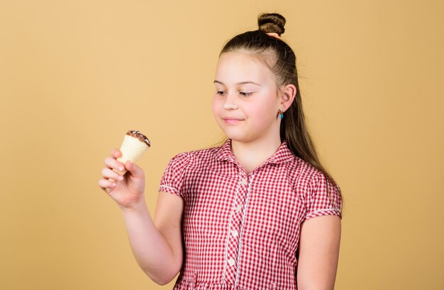 Día internacional de los niños Concepto de goloso Niña pequeña come helado fondo beige El verano está aquí Delicioso helado Infancia feliz Niño despreocupado disfruta de helado dulce