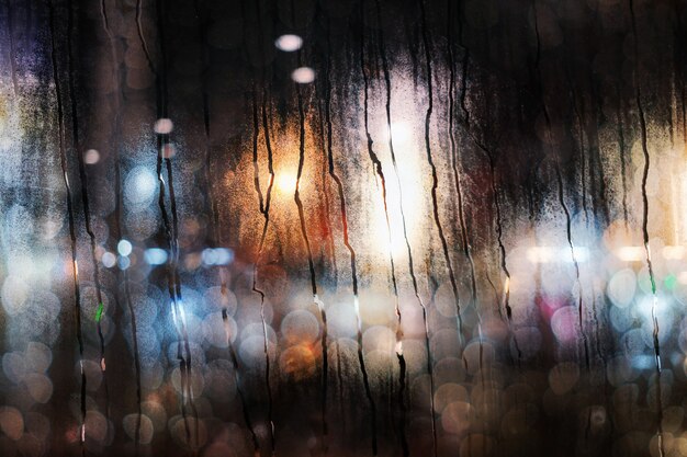 Día de lluvia en concepto de ciudad. Las gotas de lluvia en la ventana de cristal. Luces urbanas borrosas como vista exterior