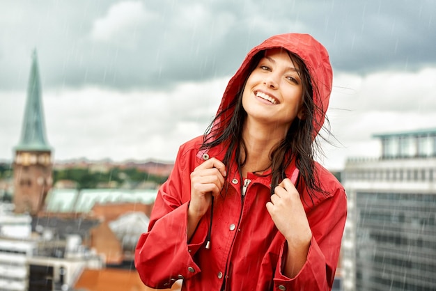 Un día lluvioso no puede bajarla Bastante joven sonriendo mientras usa un retrato impermeable rojo