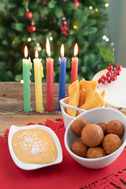 Día de la luz de las velas. Comida típica colombiana. Buñuelo, natillas y hojuelas con velas y árbol de Navidad de fondo. Fiesta tradicional colombiana. Video vertical.