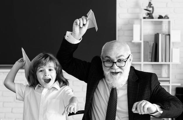 Foto día del maestro el viejo maestro sénior y el joven estudiante o escolar sostienen un avión de papel el pedagogo y el alumno se divierten