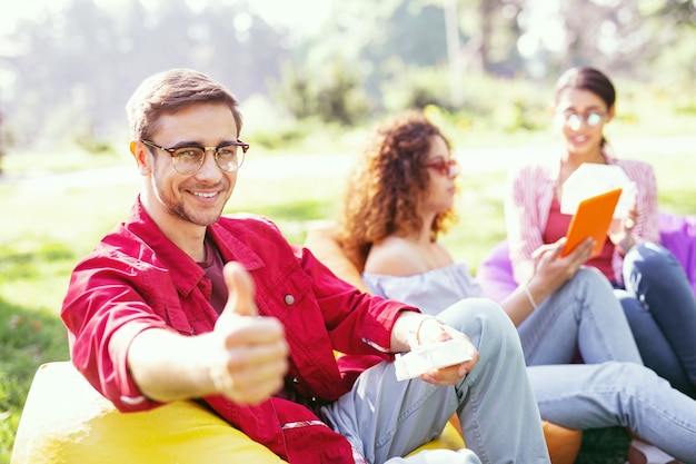 Dia maravilloso. Hombre alegre guapo sonriendo y trabajando con sus colegas al aire libre