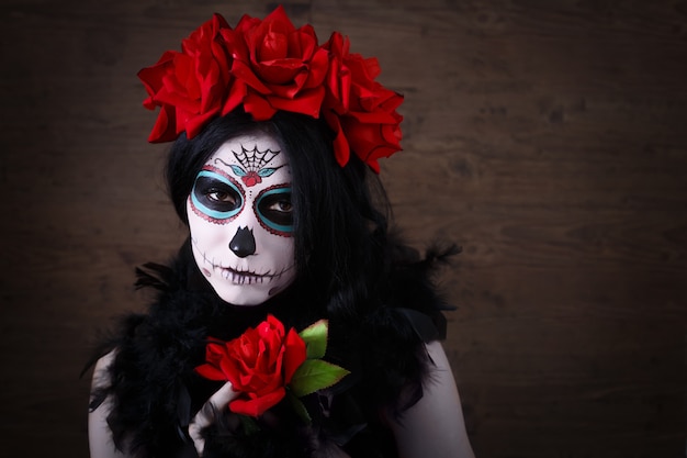 Dia de los Muertos. Festividad de Todos los Santos. Mujer joven en el día de los muertos máscara cráneo cara arte y rosa. Fondo oscuro