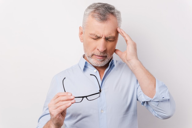 Dia muito estressante. Homem sênior frustrado com uma camisa tocando a cabeça com os dedos e mantendo os olhos fechados, enquanto se apoia em um fundo branco