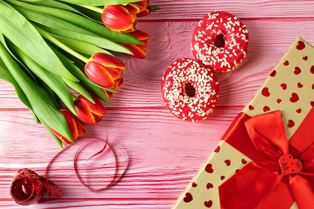 Día de la mujer, 8 de marzo, rosquillas rosadas con flores sobre una superficie rosa debajo de un árbol, caja de regalo, vista superior