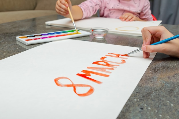 Día de la mujer, los niños dibujan con pinturas, en una hoja de papel blanca, tarjeta de felicitación.