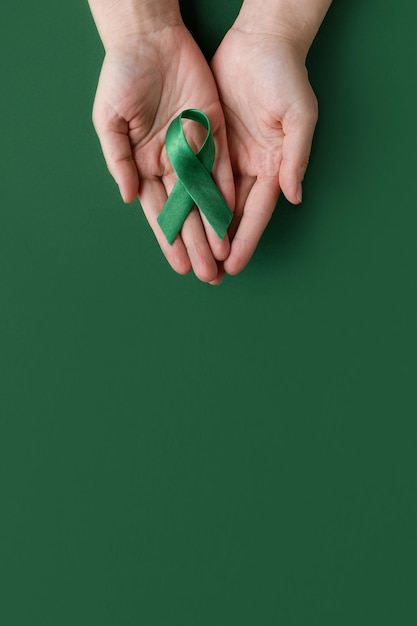 Foto dia mundial bipolar mãos adultas segurando uma fita verde sobre fundo verde dia de conscientização de saúde mental