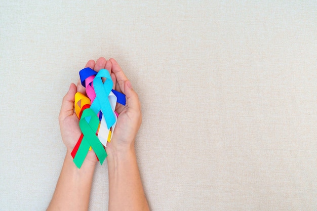 Día mundial contra el cáncer 4 de febrero Mano sosteniendo cintas azules, rojas, verdes, blancas, rosadas, azul marino y amarillas para apoyar a las personas que viven y enferman Concepto del día de la concientización sobre la salud y el autismo