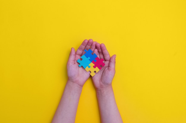 Foto dia mundial da conscientização do autismo mãos de crianças segurando quebra-cabeças coloridos em fundo amarelo