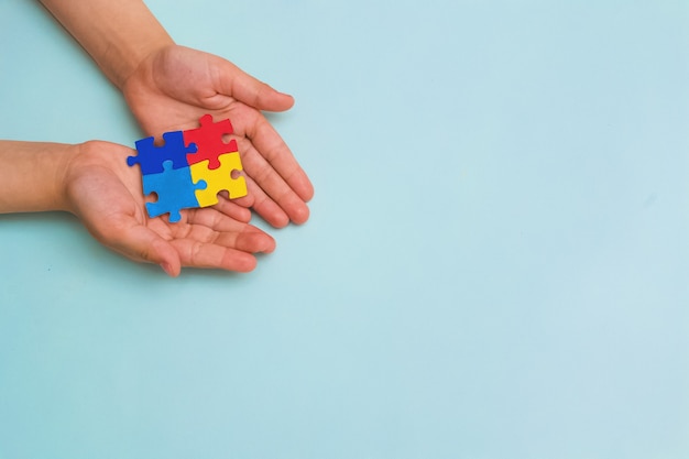 Dia Mundial da Conscientização do Autismo Mãos de uma criança segurando quebra-cabeças coloridos sobre fundo azul