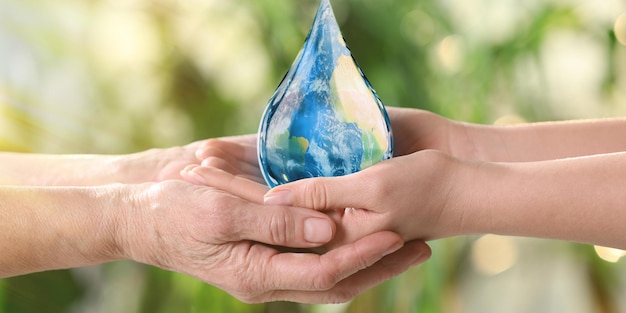 Dia Mundial da Água Mulheres jovens e idosas segurando o ícone de gota com a imagem da Terra dentro de um fundo verde desfocado fechado